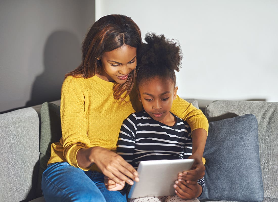 Blog - Portrait of an African American Mother and her Young Daughter Sitting on the Sofa at Home While Reading on a Tablet